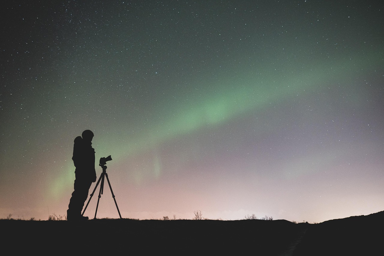 Silhouettes de photographes et trépieds face à une aurore boréale et un ciel étoilé