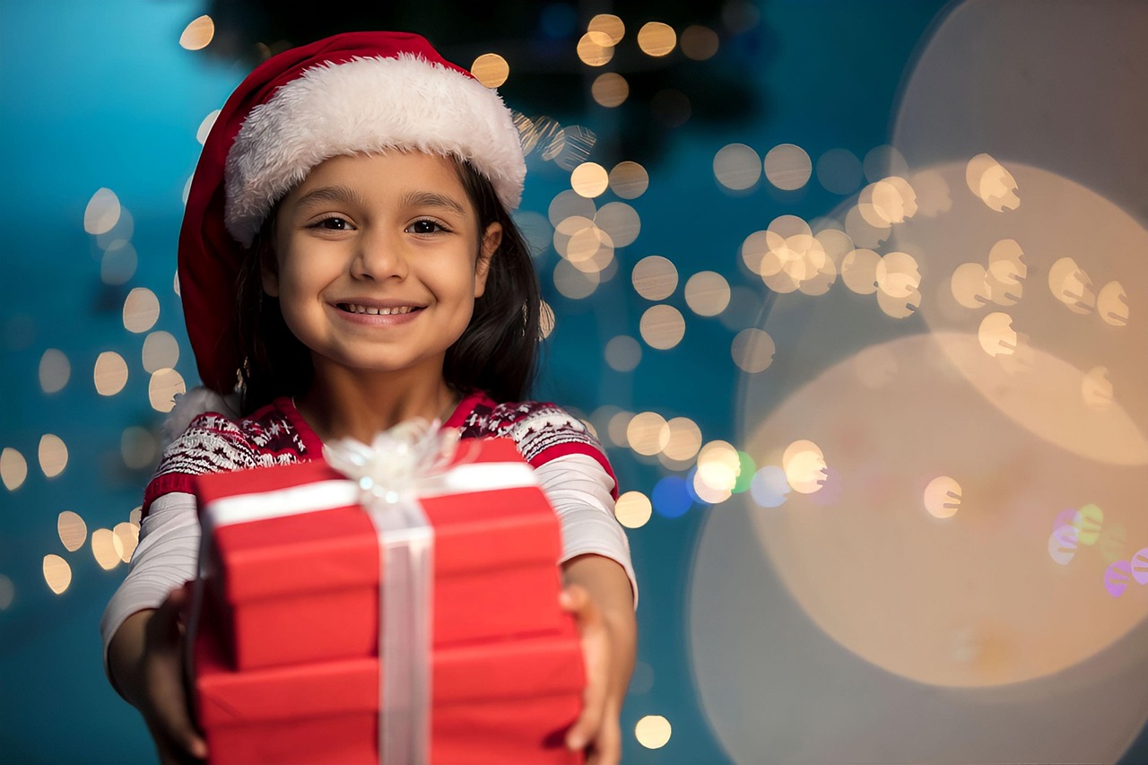 Enfant en bonnet de Père Noël tendant un cadeau devant des guirlandes lumineuses