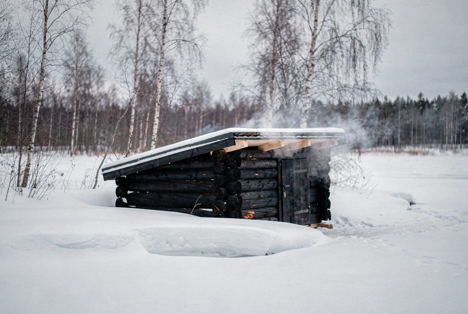 Petit sauna fumé en rondins noircis au bord d'un lac gelé de Laponie finlandaise